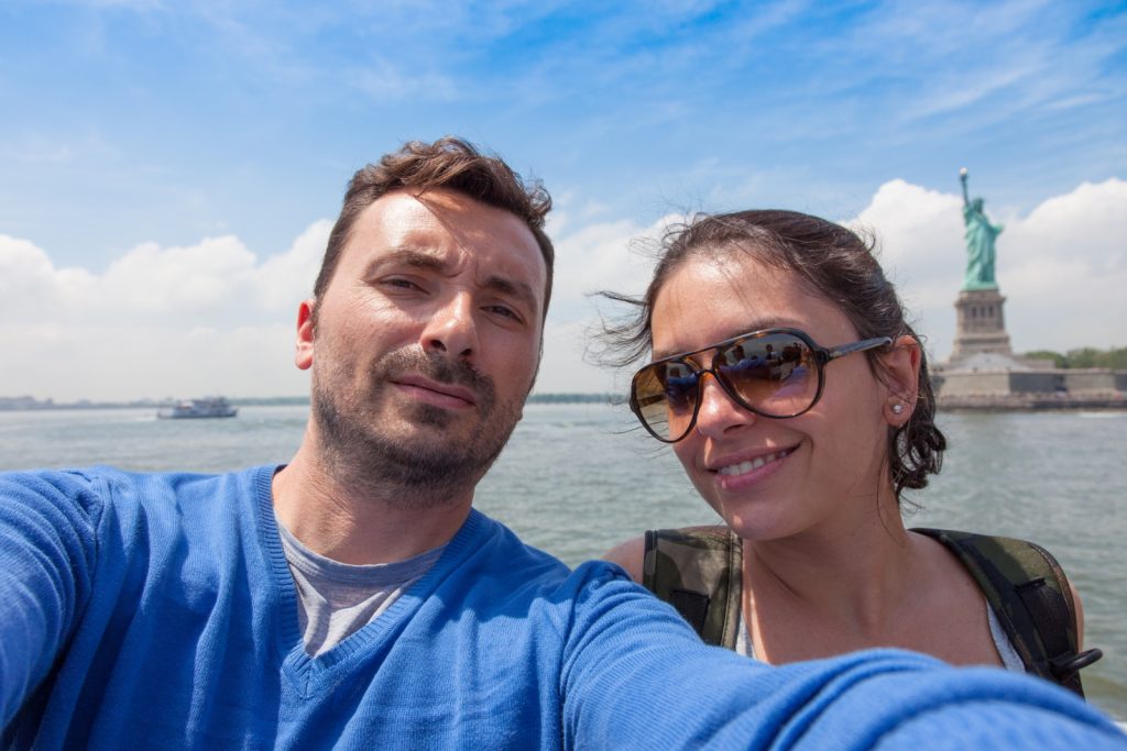 couple taking selfie in front of the Statue of Liberty